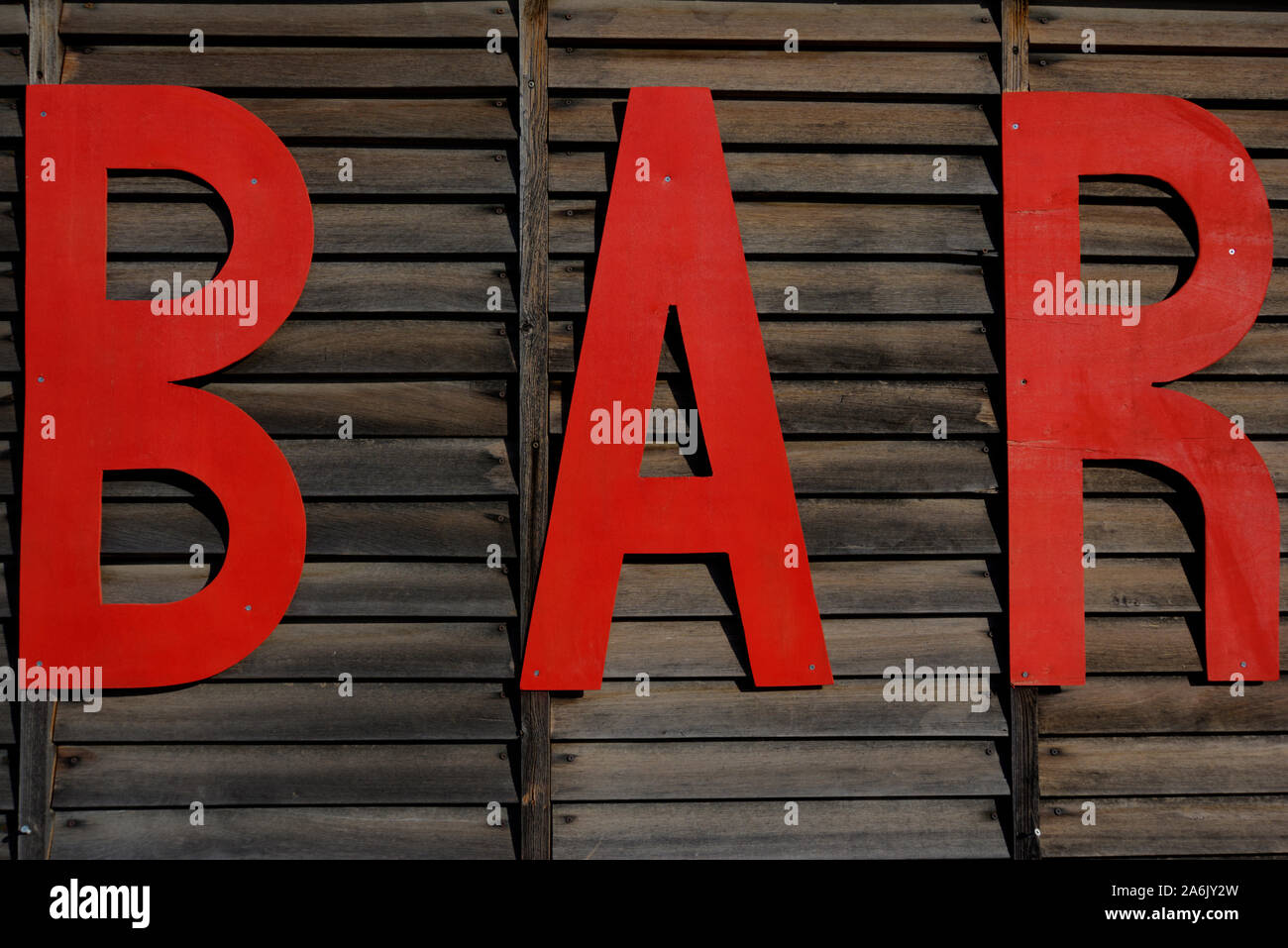 The word BAR in large red capital letters on a brown wooden slatted fence Stock Photo