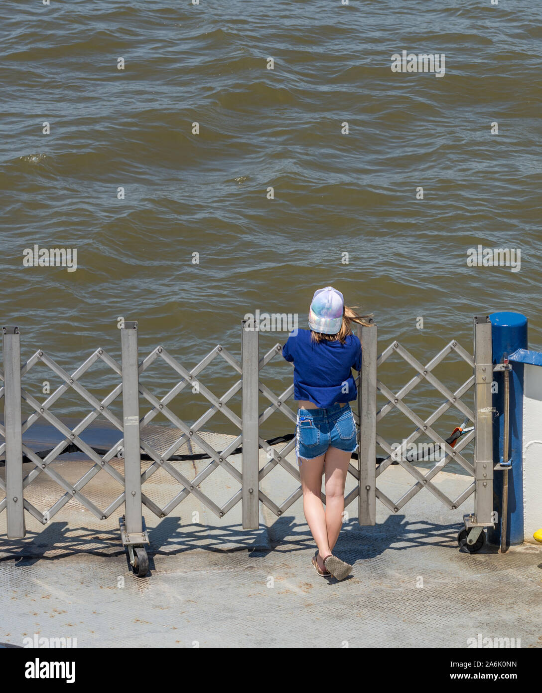 Young woman in shorts and sandals standing at ferry gate looking at water Stock Photo