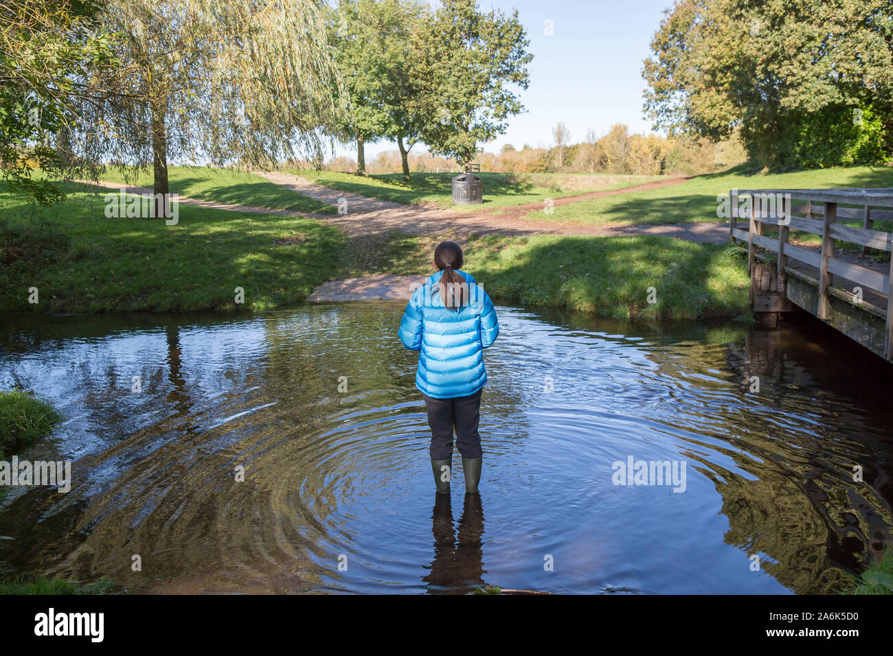 After the rain: rear view of a female (wearing wellies) isolated outdoors in the autumn sunshine standing in water after days of continual rain in the UK. Stock Photo