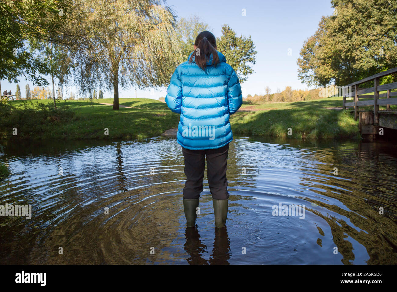 After the rain: rear view of female wearing wellies isolated outdoors in autumn sunshine standing in water after days of continual rain in the UK. Stock Photo