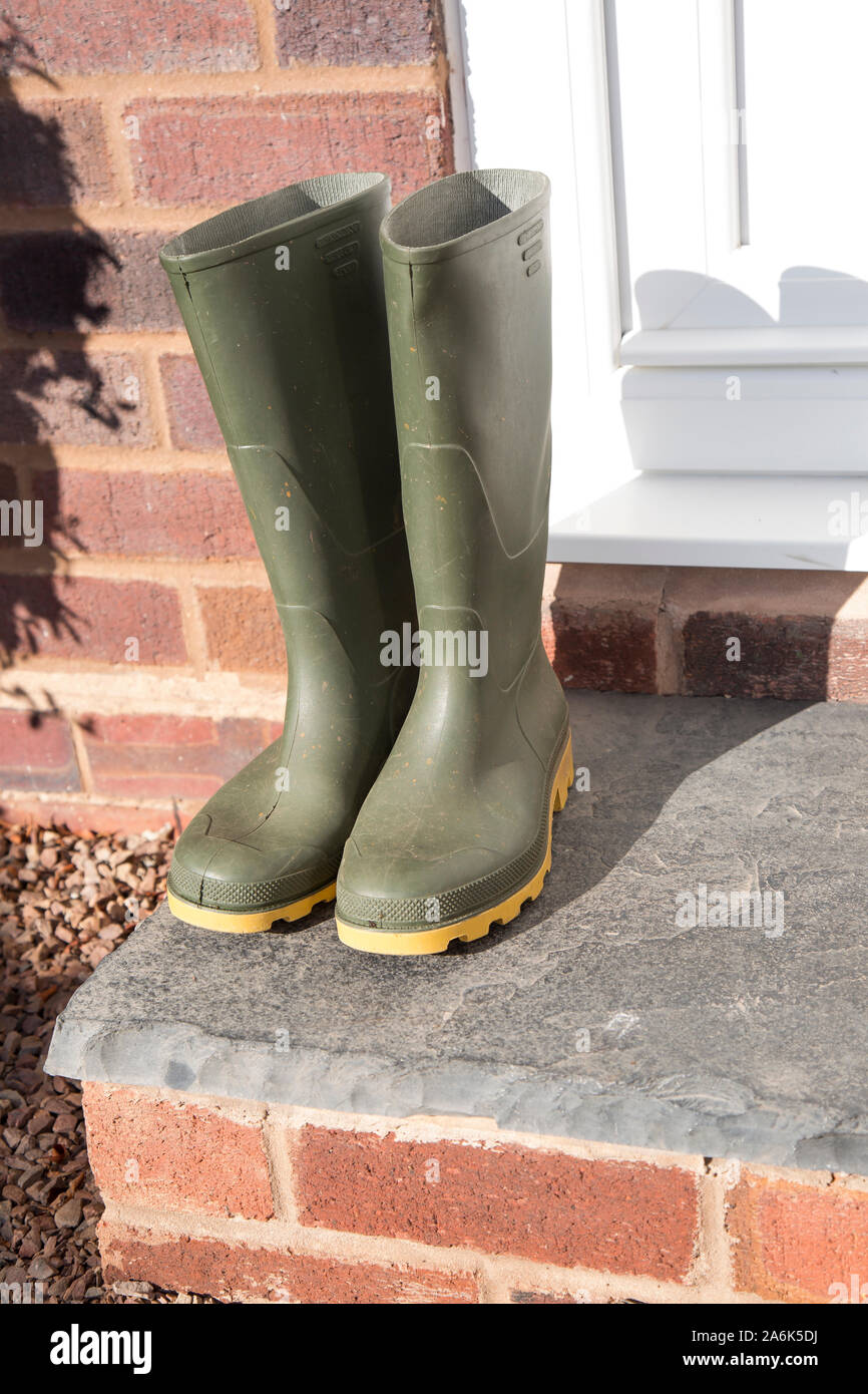 Pair of green wellington boots (front view) isolated outdoors on the front doorstep of UK residential property after a walk in the autumn sunshine. Stock Photo