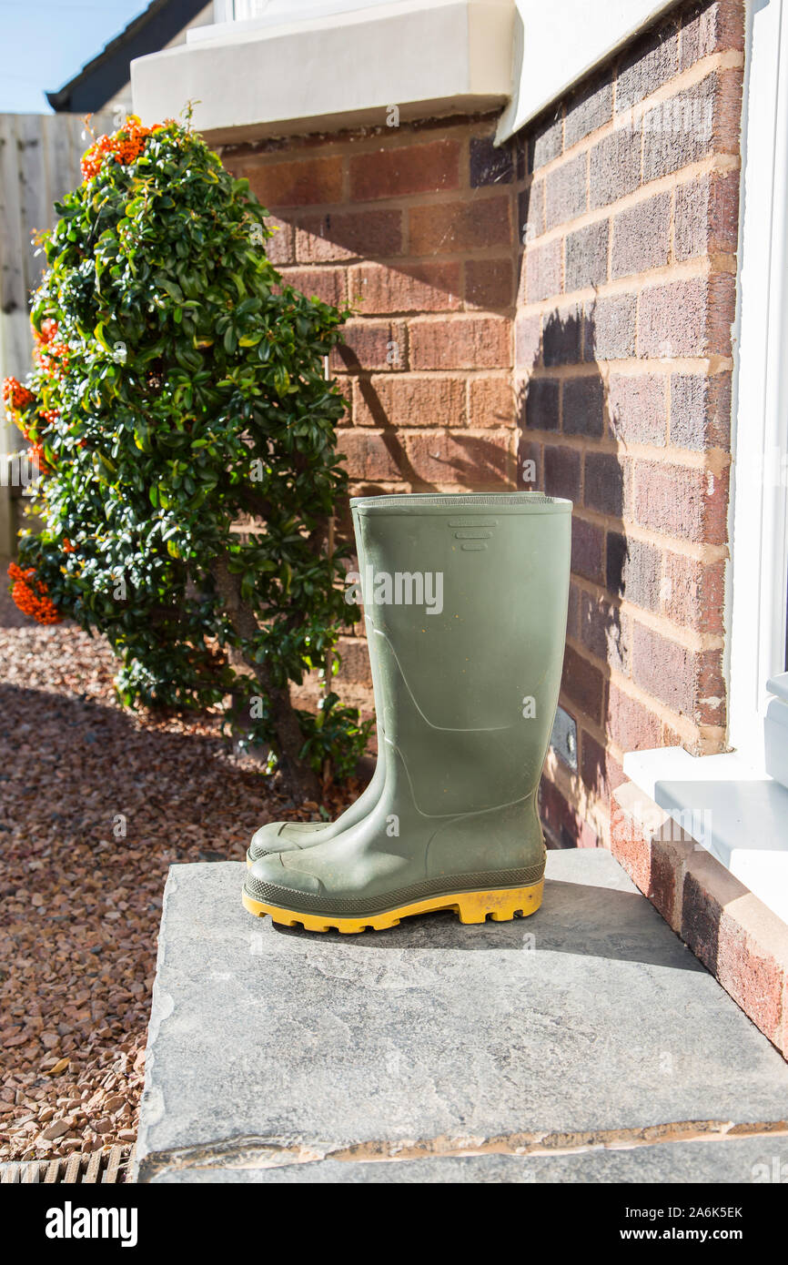 Pair of sunlit, green wellington boots (side view) isolated outdoors on a UK front doorstep after a walk in the autumn sunshine. Stock Photo