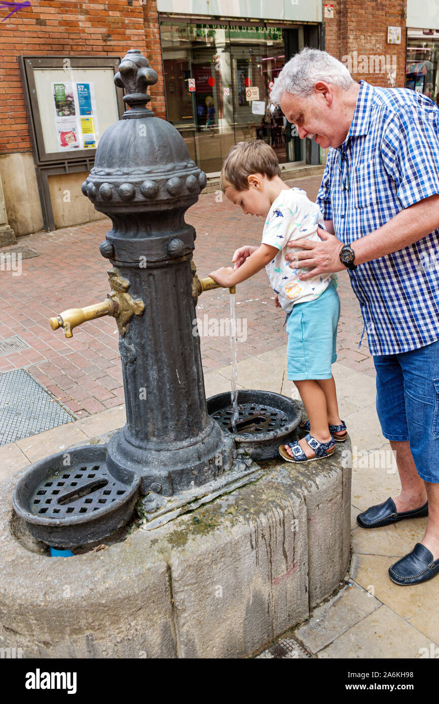 Barcelona Spain,Catalonia El Clot,old style public water fountain pumps,potable drinking water,man,boy,grandfather,grandson,Hispanic,ES190820050 Stock Photo