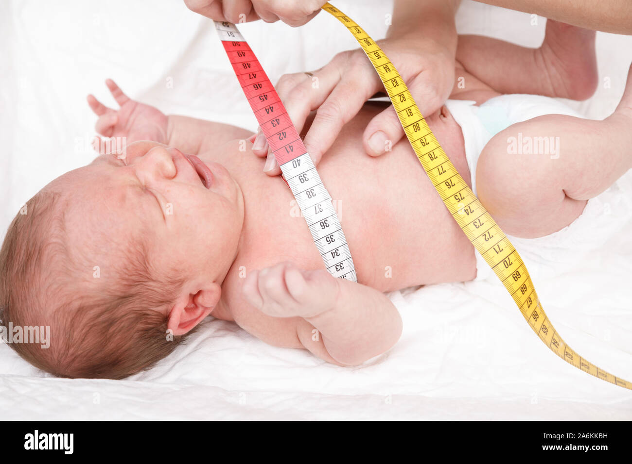 Pediatrician examines two week old baby. Doctor using measurement tape checking newborn's chest size. Newborn check-up concept Stock Photo