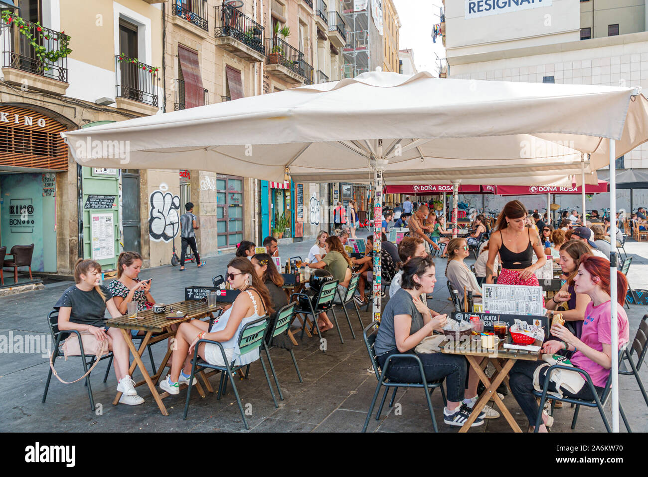Barcelona Spain,Catalonia Ciutat Vella,El Raval,Kino, restaurant,outside table,umbrella,busy,al fresco,dining,man,woman,young adult,students,waitress, Stock Photo
