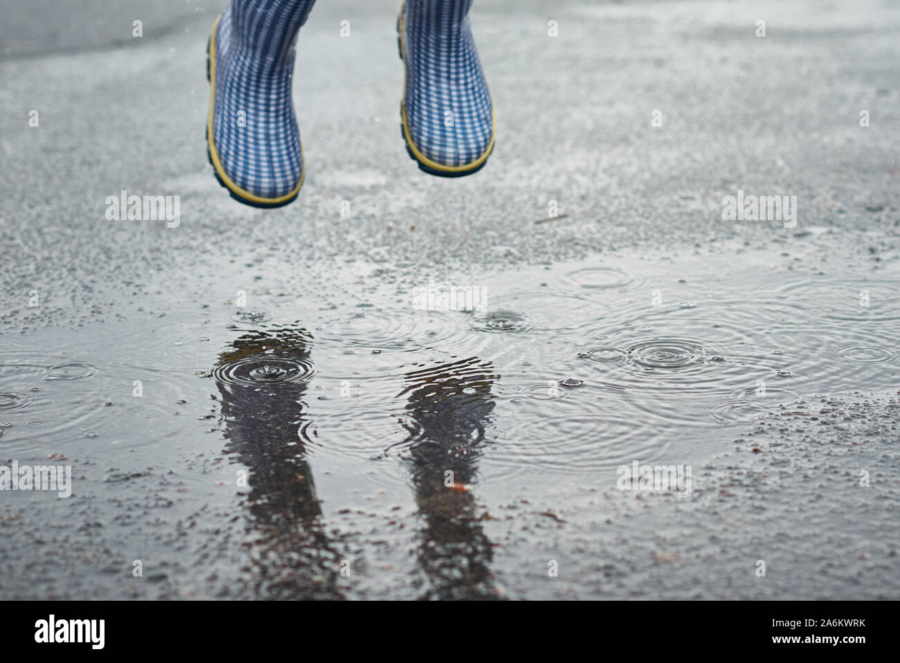 child in blue rubber boots jumping over puddle in the rain Stock Photo ...