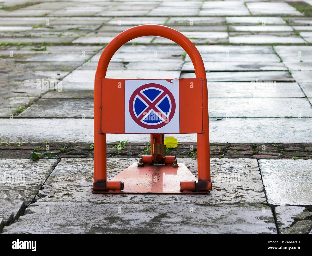 Portable road sign no stopping or parking on an orange car parking lock device over wet concrete slabs near building. Traffic rules, prohibitory sign Stock Photo