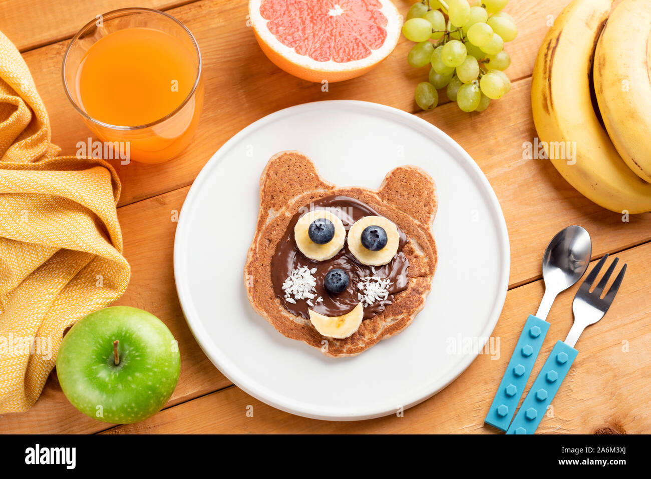 Funny breakfast pancake for kids. Food art. Childhood motherhood concept. Pancake with chocolate spread, banana and blueberry shaped as cute funny ani Stock Photo