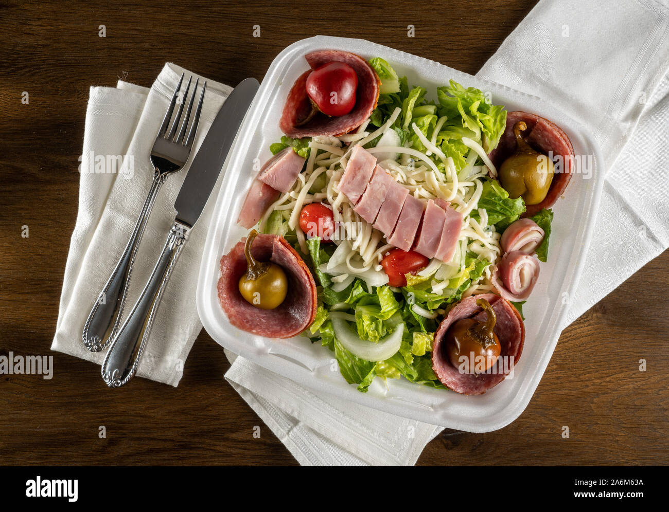 Flat lay view of antipasta salad with ham, salami peppers and lettuce in a delivery plastic box and eaten at home with napkin Stock Photo
