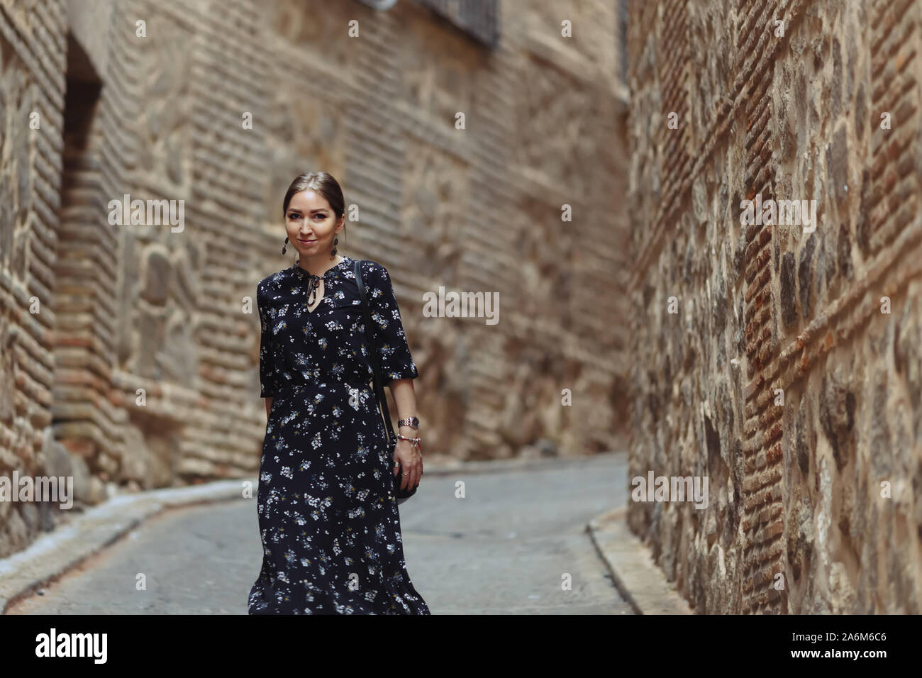 Fashion portrait of young beautiful girl posing on the old town street. Ancient stone streets with women tourist in Toledo, Spain. Stock Photo