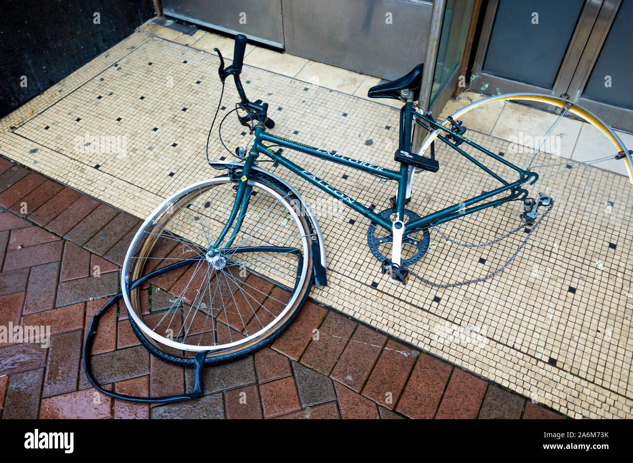 A ladies Falcon bicycle securely locked to a post in a shop doorway, is lying down has a damaged front wheel and missing probably stolen Stock Photo