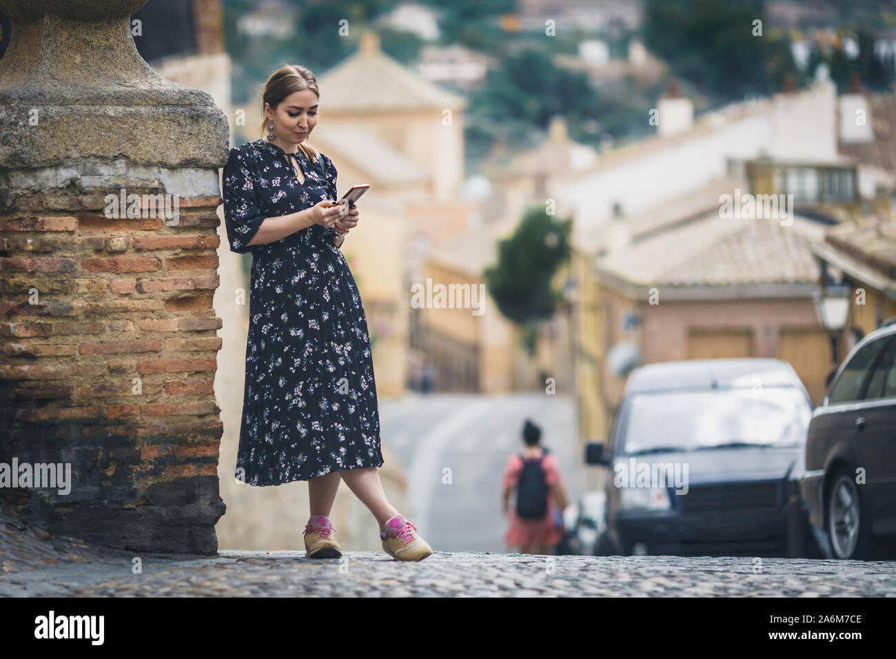 Pretty young woman in a black dress using smartphone at old town street. Travel by Europe. Stock Photo