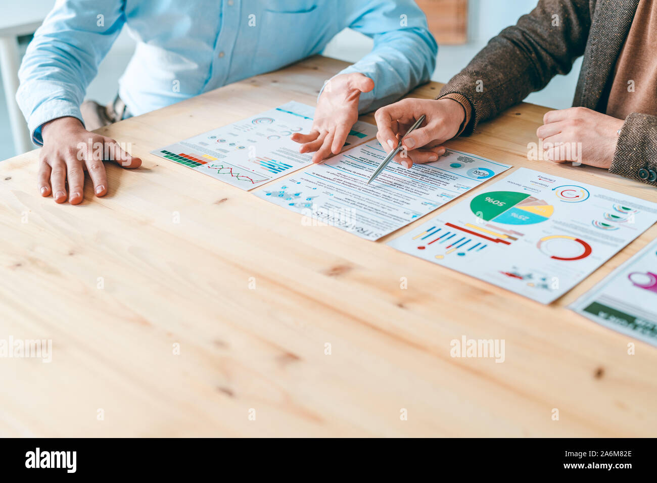 Two young businessmen sitting by wooden table while discussing documents Stock Photo