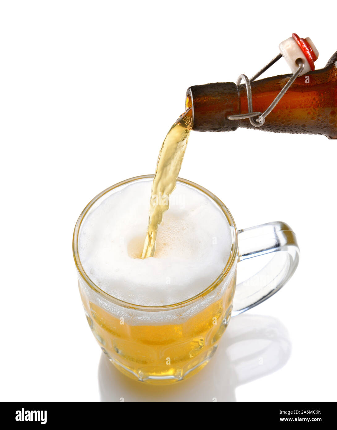 Cold beer pouring from a bottle into a mug on a white background with reflection. Stock Photo