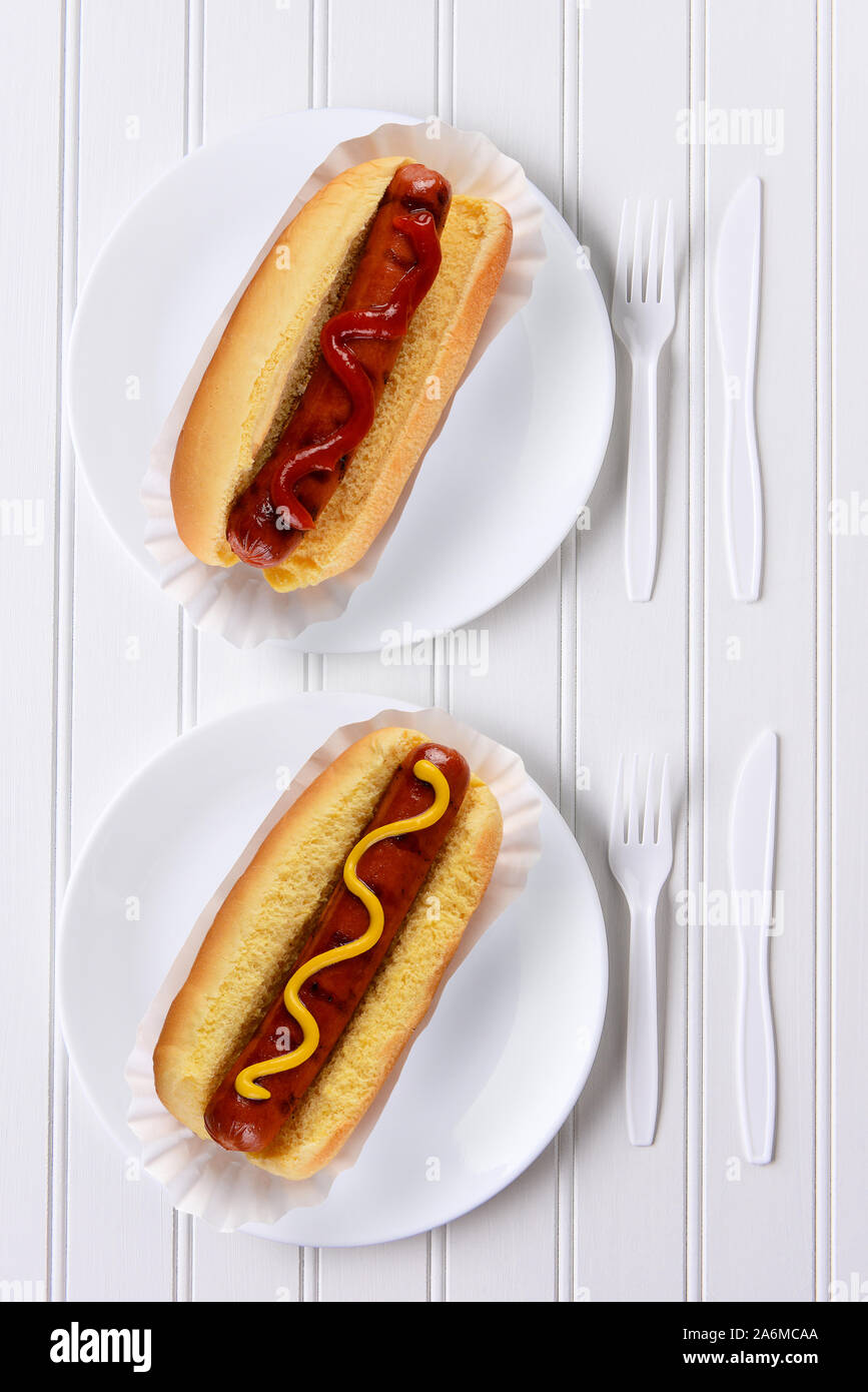 Top view of an all white place setting with hot dogs one with ketchup, one with mustard. Stock Photo