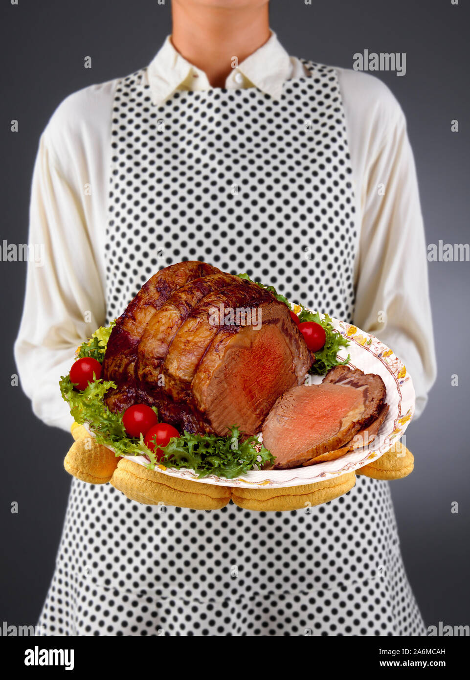 Closeup of a homemaker in an apron and oven mitts holding a Platter of Roast Beef, sliced with garnish. Stock Photo