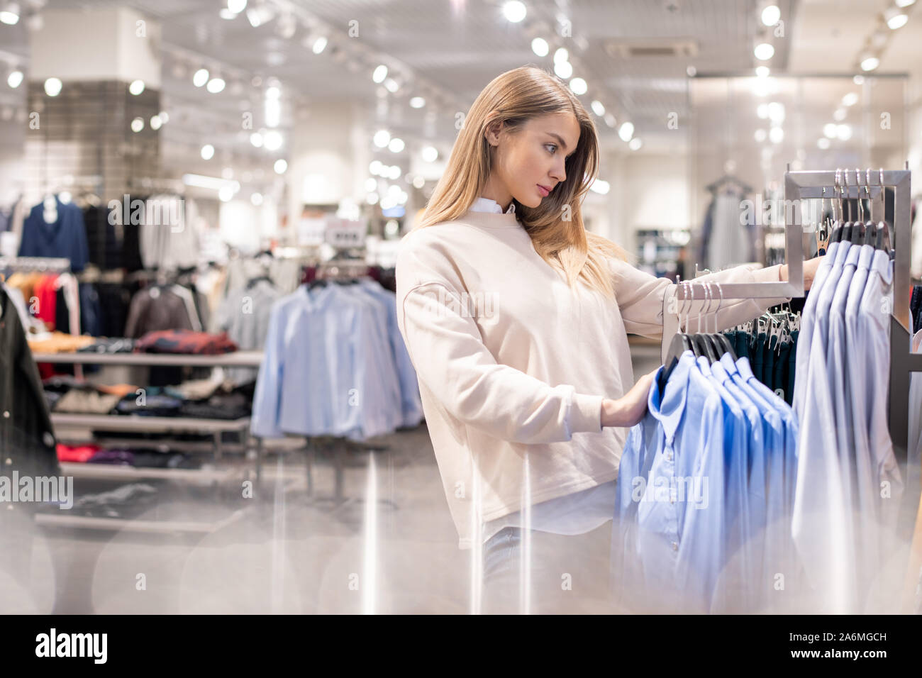 Young female shopaholic standing by one of racks in casualwear department Stock Photo