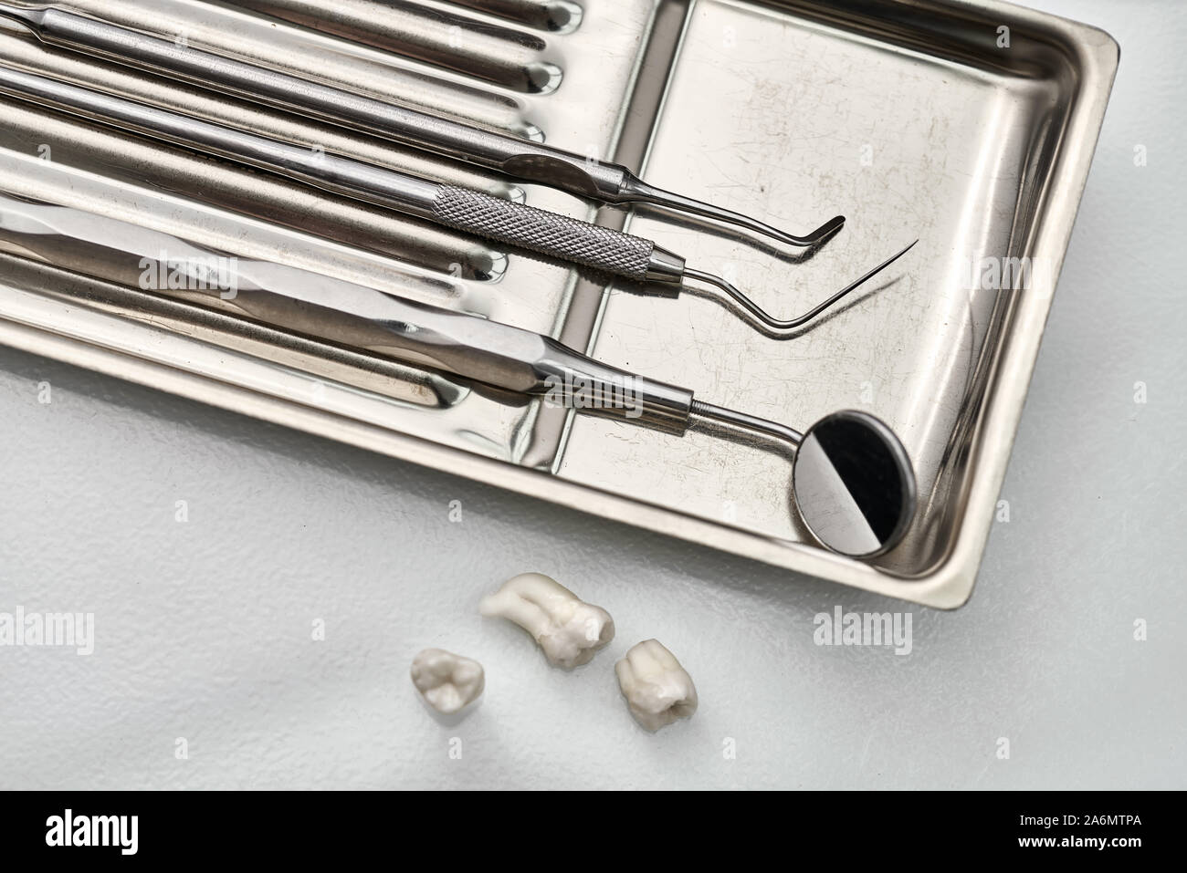 Stainless steel medical tray with dental instruments (mirror, probe, scrapers) and three extracted molar teeth next to it. Closeup horizontal photo. Stock Photo