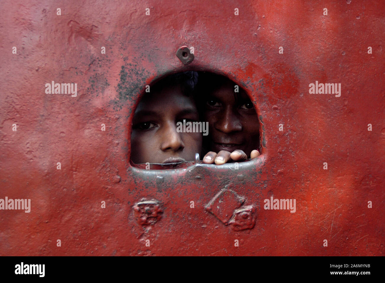 Workers looking through a hole on the gate of Nippun Garments Factory, in Tongi, Gazipur, Bangladesh. October 31, 2009. Stock Photo