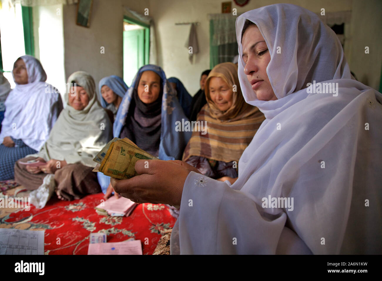 Sitting in front of a group of women who attend a VO (Village Organization) meeting, a group leader counts Afghani notes in Kucha-e-Abul Fazal neighbourhood in Kabul, the capital of Afghanistan. Stock Photo