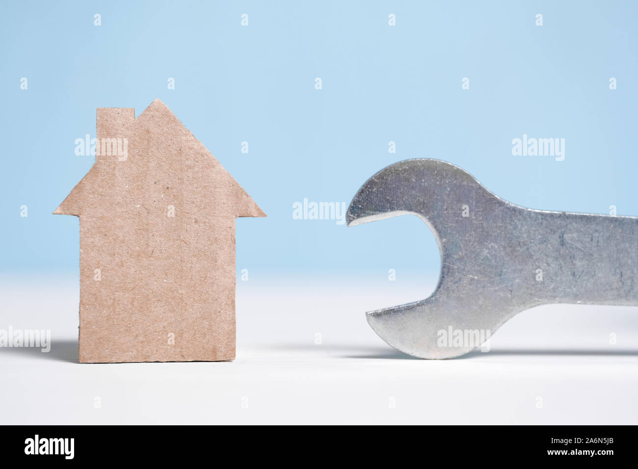 Abstract cardboard house next to a wrench. Real estate repair concept. Close up. Stock Photo