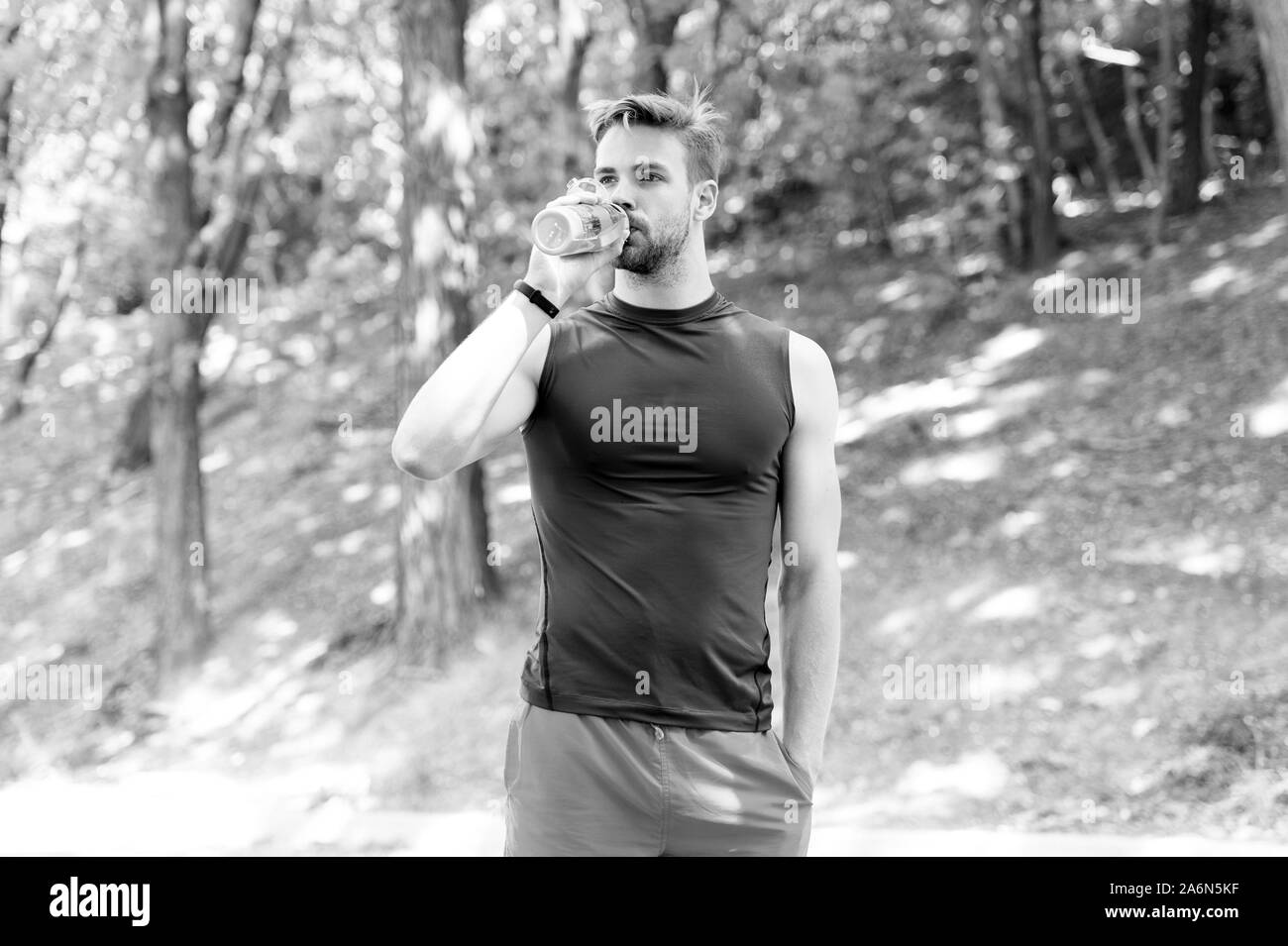 The water has a major role in sports. Thirsty sportsman drinking pure water on hot summer day. Fit athlete having a drink from water bottle during training outdoor. Keeping body water balance. Stock Photo