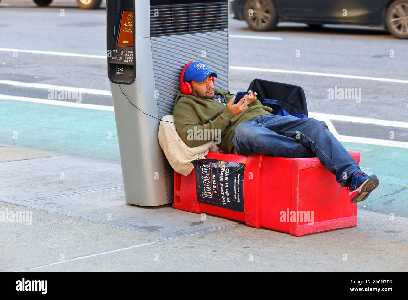 Person with headphones on charging their phone at a LinkNYC public WiFi hotspot in NYC while