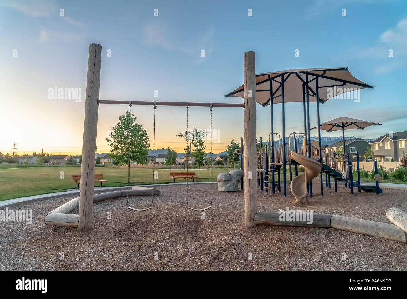 Childrens playground at a park with swings slides and umbrellas viewed at sunset Stock Photo