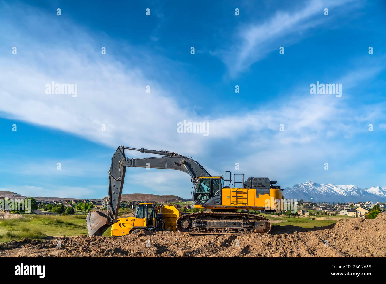 Excavator at a construction site with mountain homes and cloudy sky ...