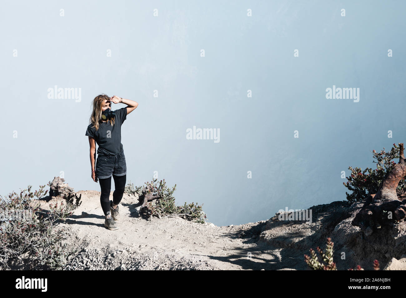 Young woman in protective mask on summit of active volcano Kawah Ijen above crater acid lake with poisonous fume. Popular travel destination. Stock Photo