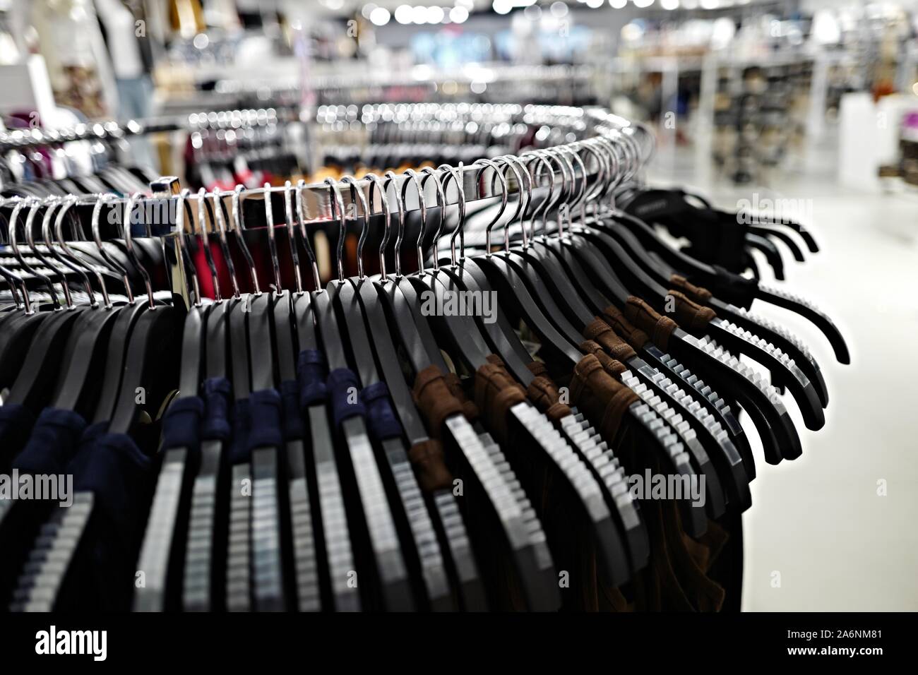 a round display rack of clothing hanging from black plastic hangers inside a brightly lit store Stock Photo