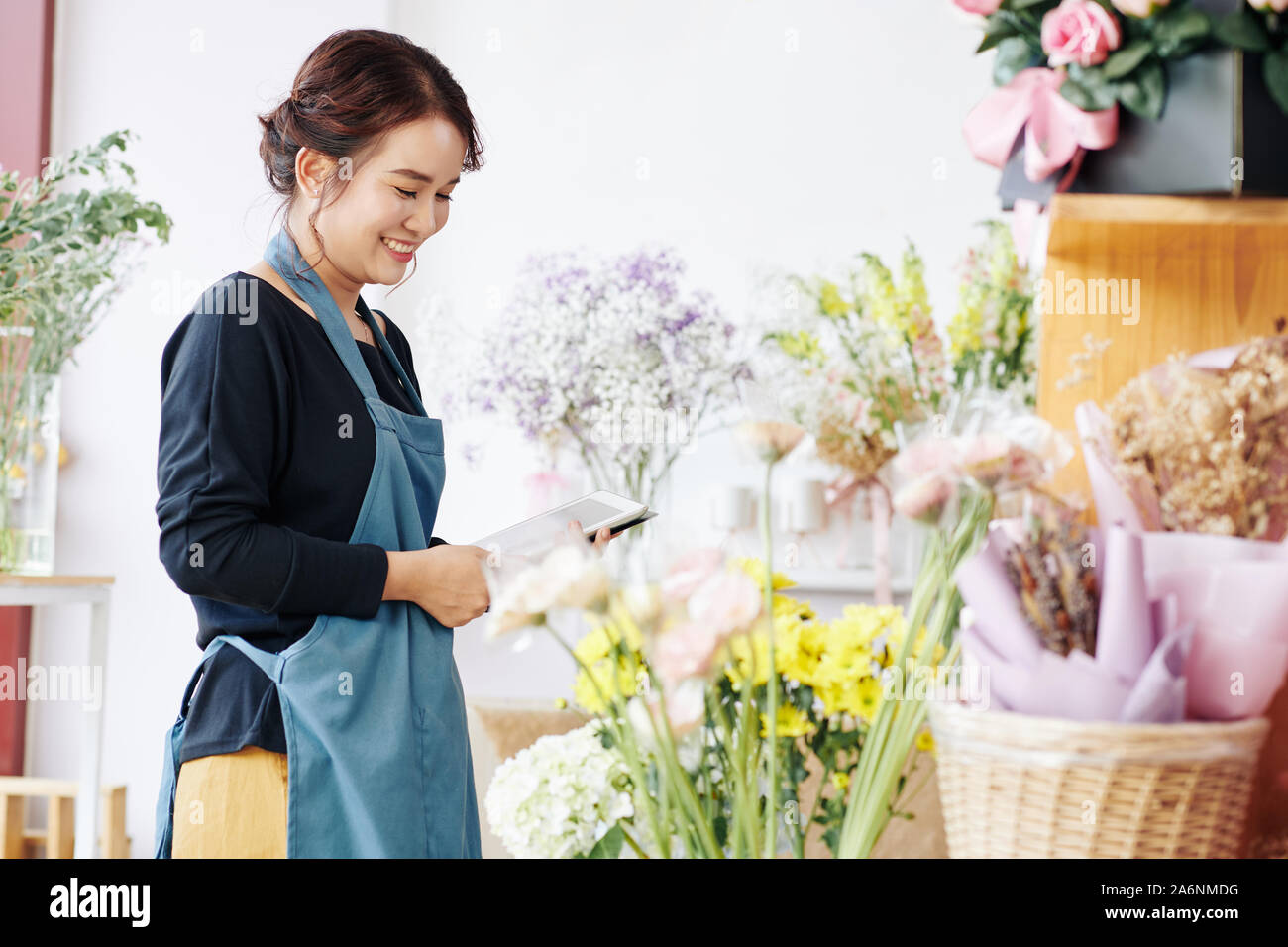 Pretty smiling young florist using tablet computer when checking flowers in her store Stock Photo