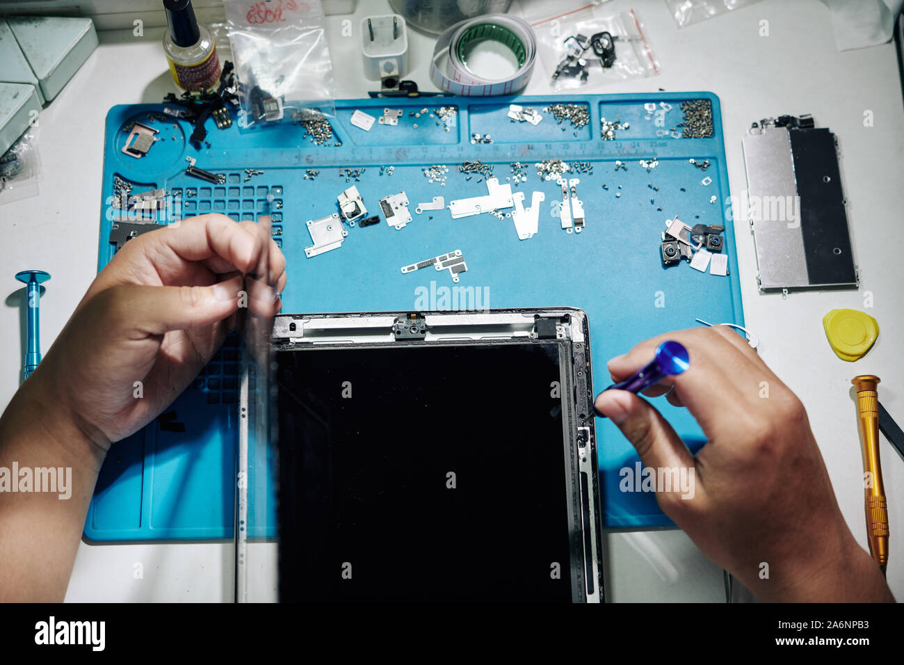 Repairman using tweezers and screwdriver when removing screen of tablet