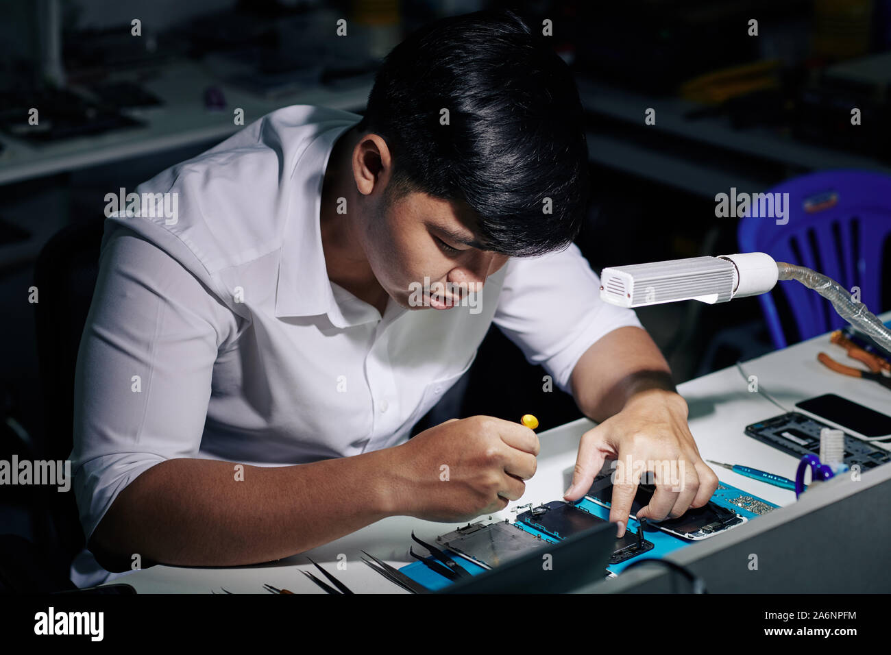 Concentrated young Vietnamese repairman using screwdriver to assemble