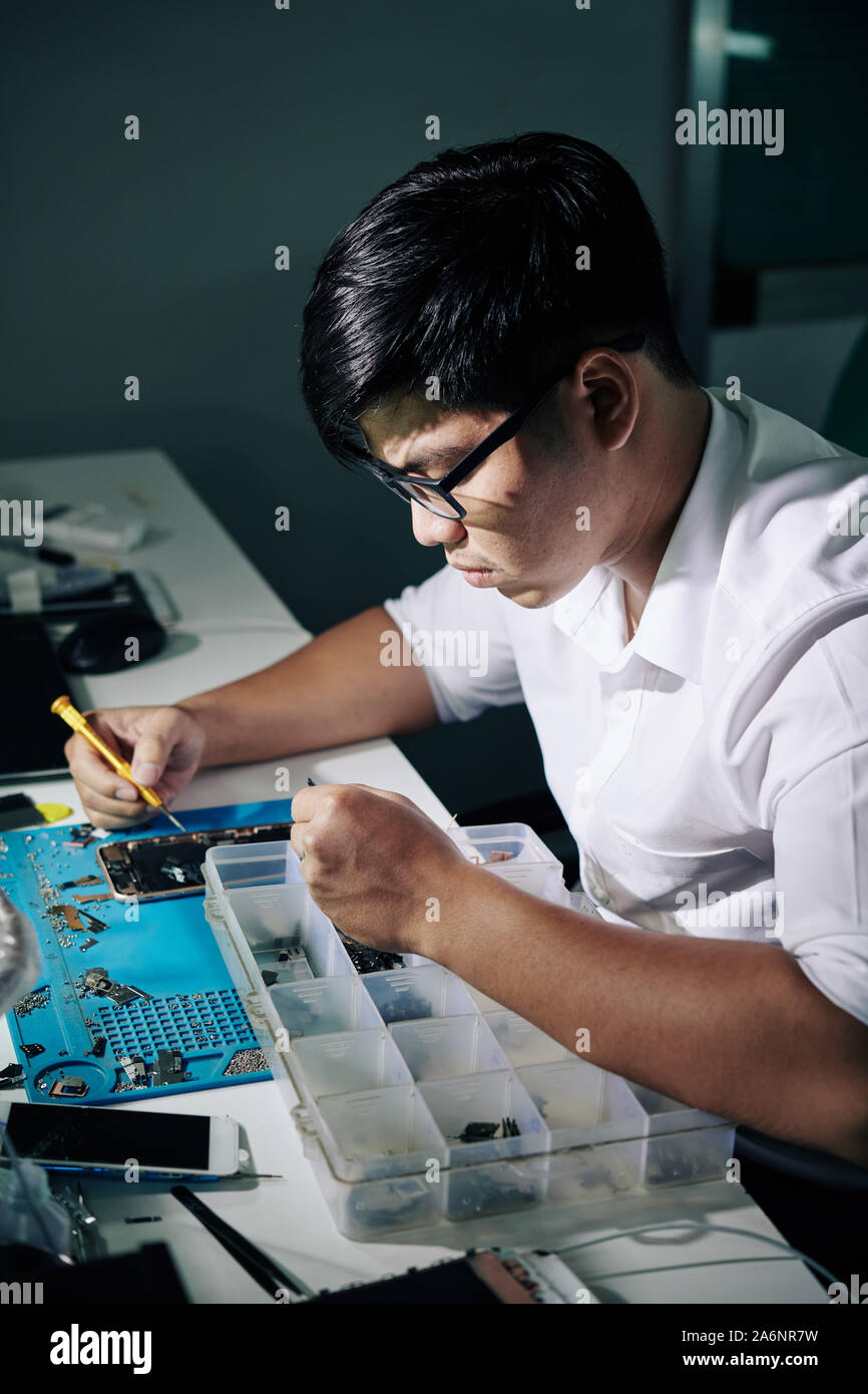 Professional Vietnamese repairman concentrated on fixing smartphone Stock Photo