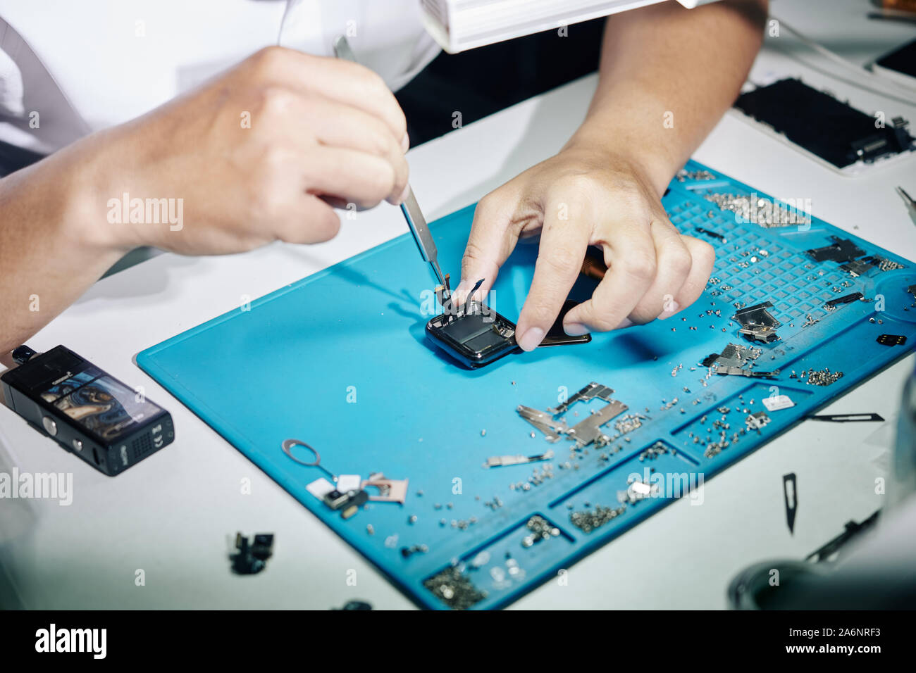 Hands of repairman removing back panel of smartwatch when fixing it