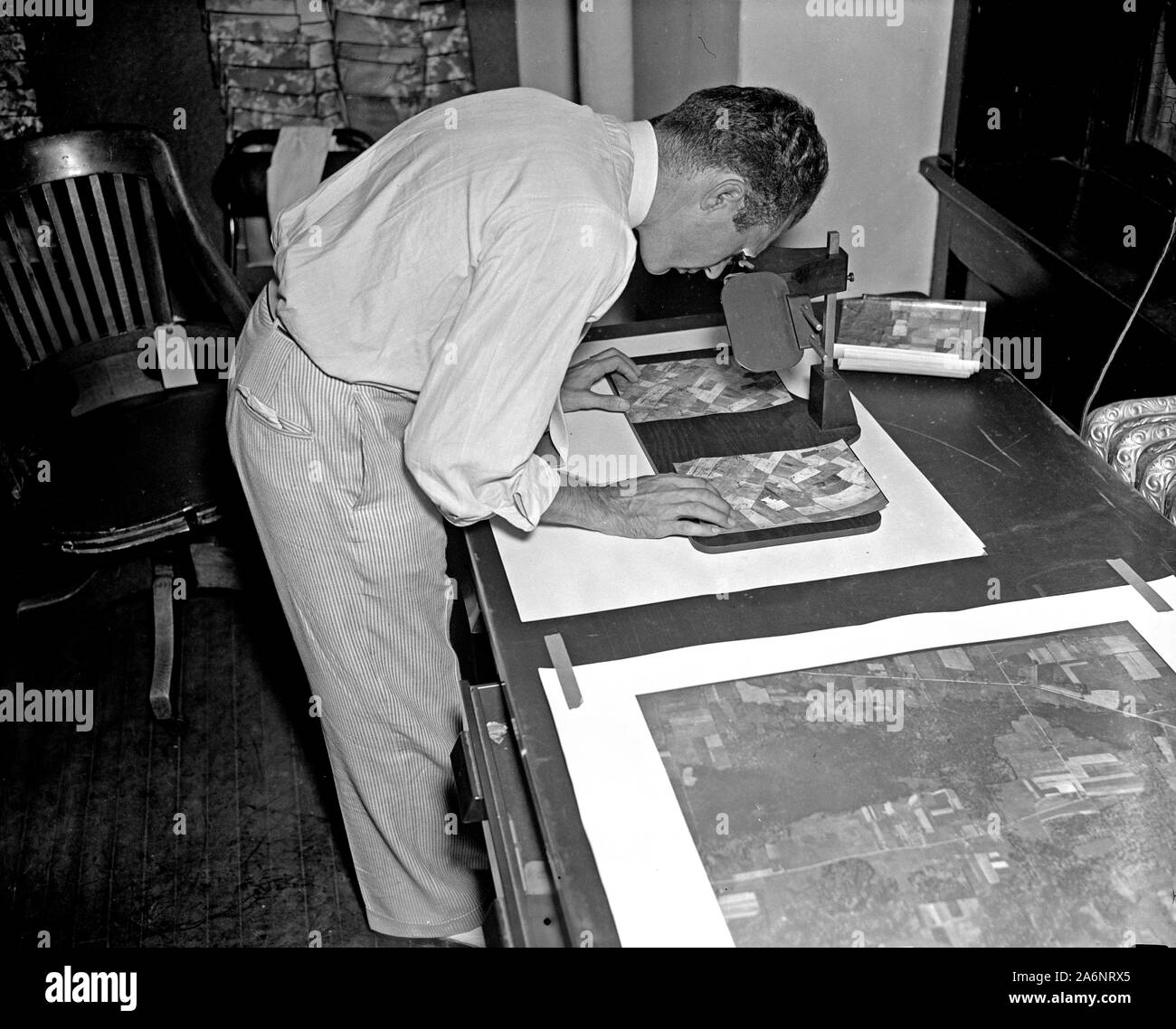 A worker is shown making a stereoscopic examination of the finished photographic prints to determine the relief or elevation of land surface for a map of the United States ca. 1937 Stock Photo