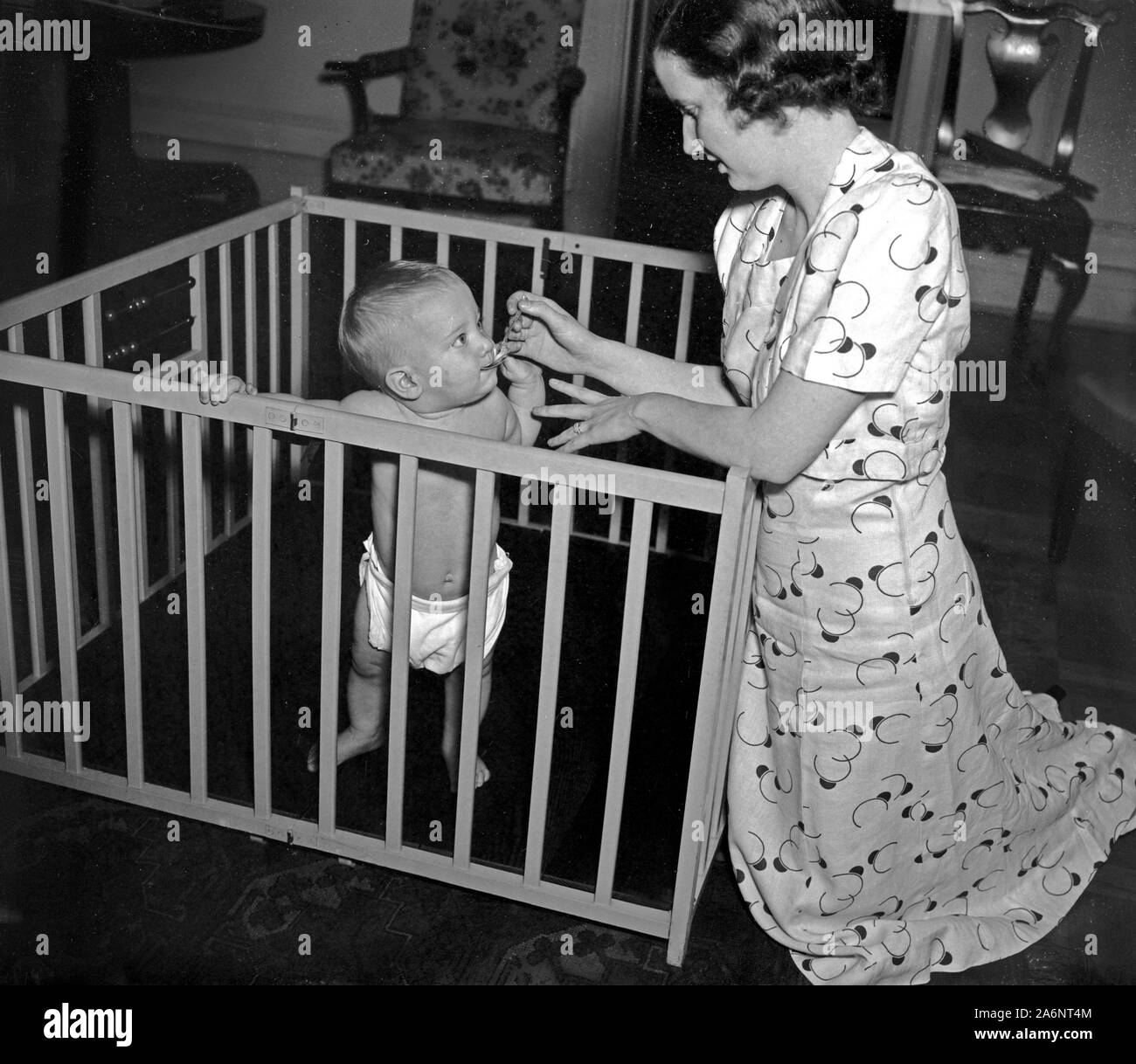 Mother feeding a baby while in a play pen ca. 1937 Stock Photo Alamy
