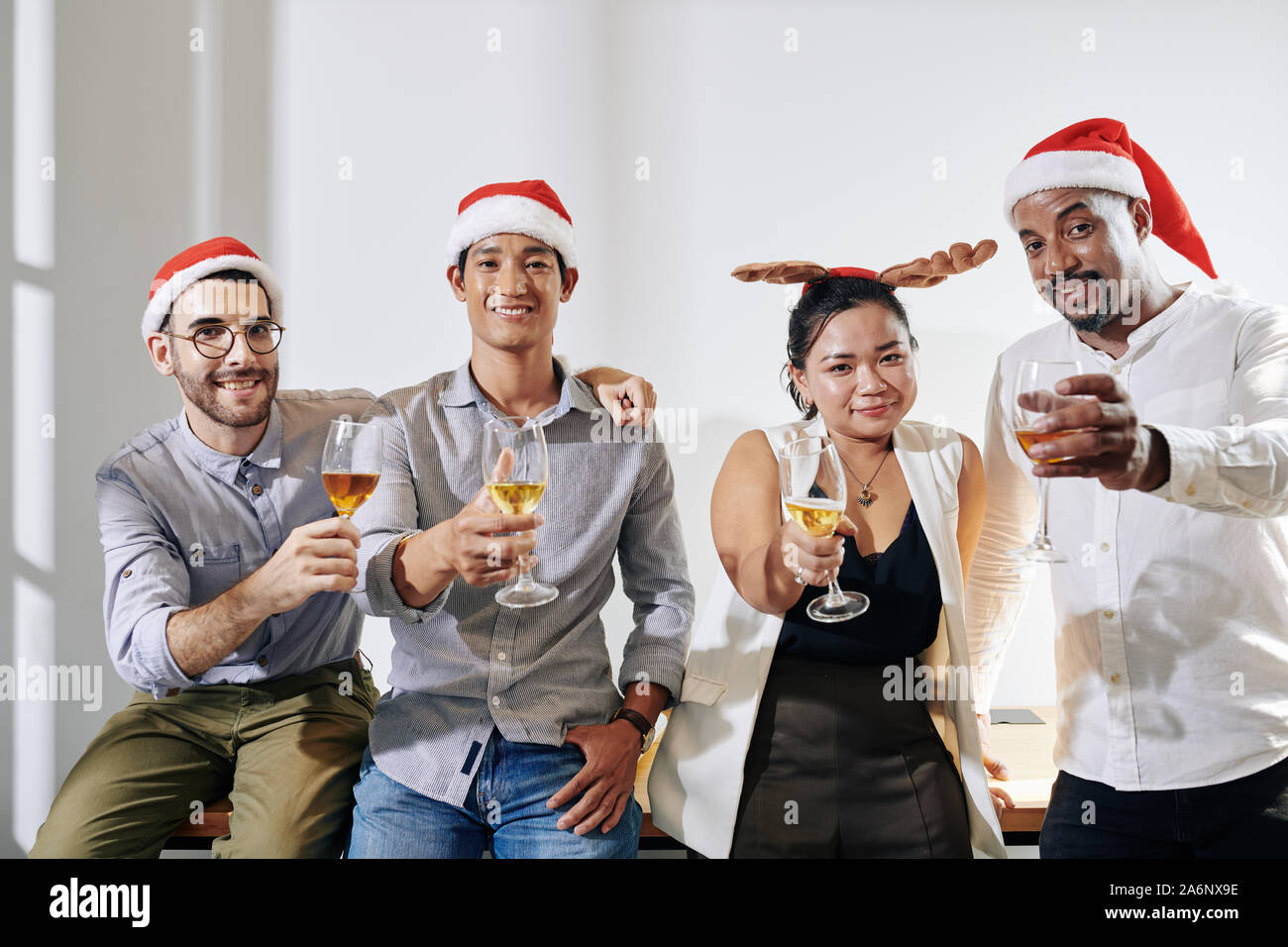 Happy young business people in Christmas hats raising hands with champagne glasses and smiling at camera Stock Photo