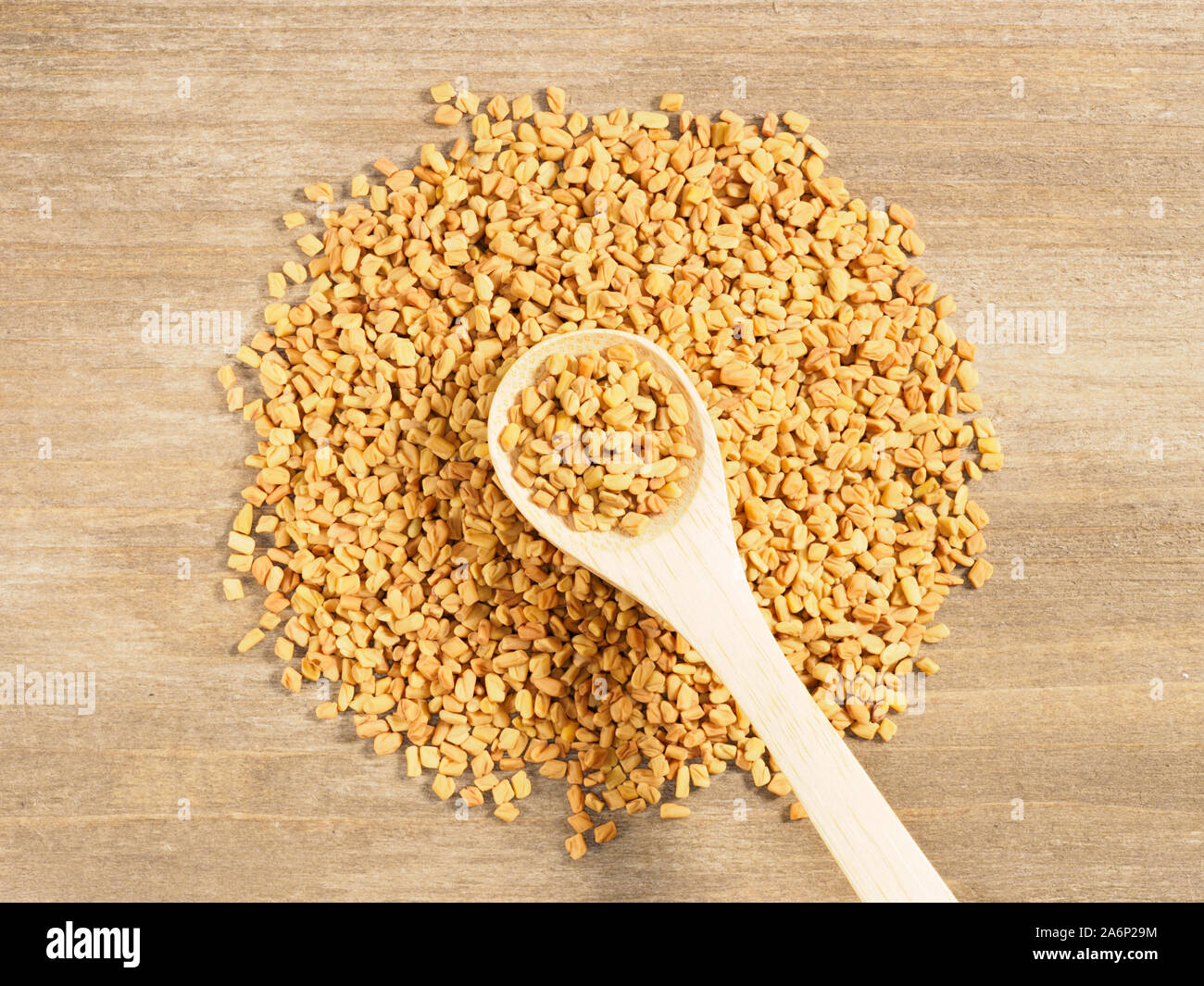 Fenugreek on a brown wooden background and in spoon. Indian cuisine, ayurveda, naturopathy, modern apothecary concept Stock Photo