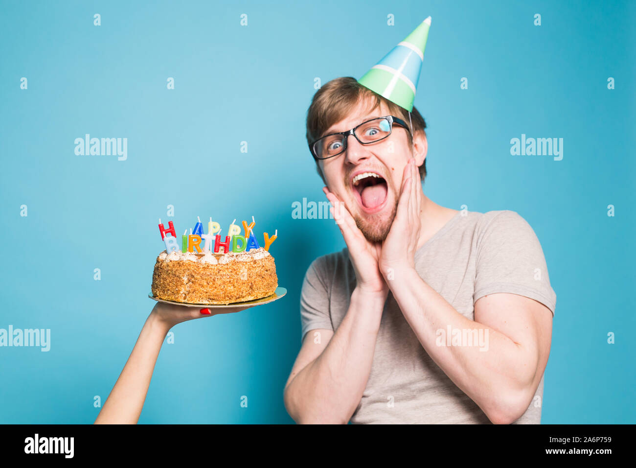 Crazy funny positive guy hipster with a happy birthday cake standing on a  blue background. Concept of jokes and holiday greetings Stock Photo - Alamy