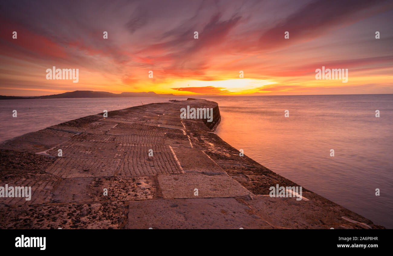 Lyme Regis, Dorset, UK. 28th Oct, 2019. UK Weather: Beautiful sunrise at the Cobb Lyme Regis. The sky over the historic Cobb wall glows with vibrant colour on a chilly autumnal morning. Credit: Celia McMahon/Alamy Live News Stock Photo