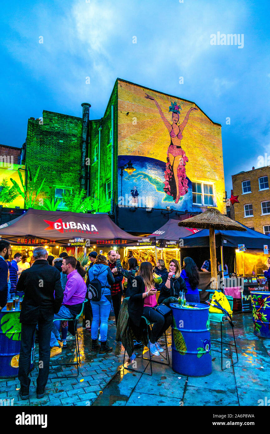 People eating, drinking and socialising at the Lower Marsh Market near Waterloo, mural on the wall of Cubana Restaurant & Cocktail Bar, London, UK Stock Photo