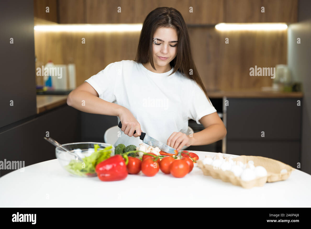 young beautiful woman chopping tomatoes cooking breakfast in the kitchen looking happy Stock Photo