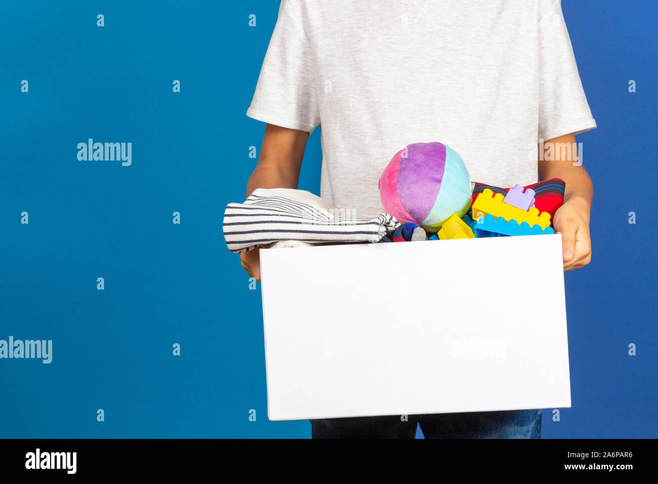 Donation concept. Kid hands holding donate box full of books, clothes