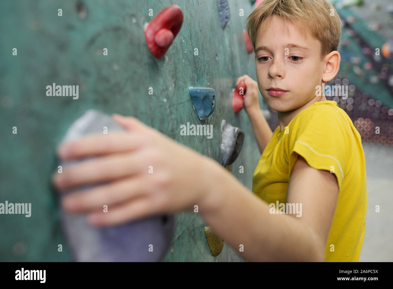 Young schoolboy in yellow t-shirt holding by small rocks on climbing wall Stock Photo