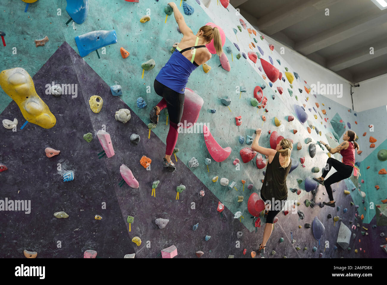 Three young sporty women in activewear grabbing by rocks on climbing equipment Stock Photo