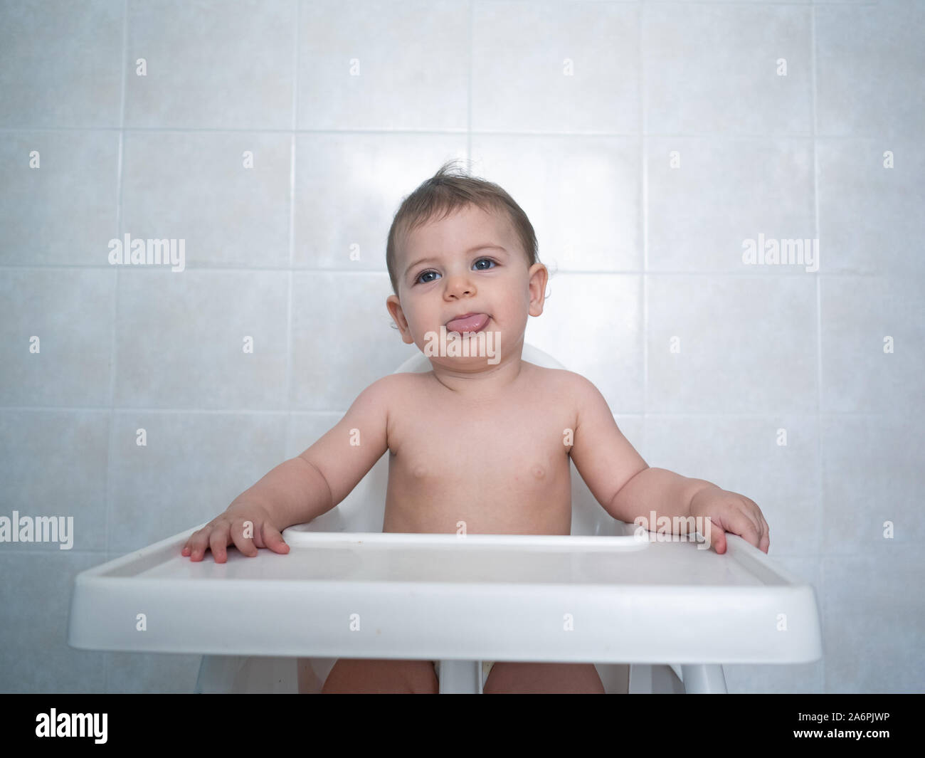 1 year old female baby sits in a high chair waiting for her meal Stock Photo