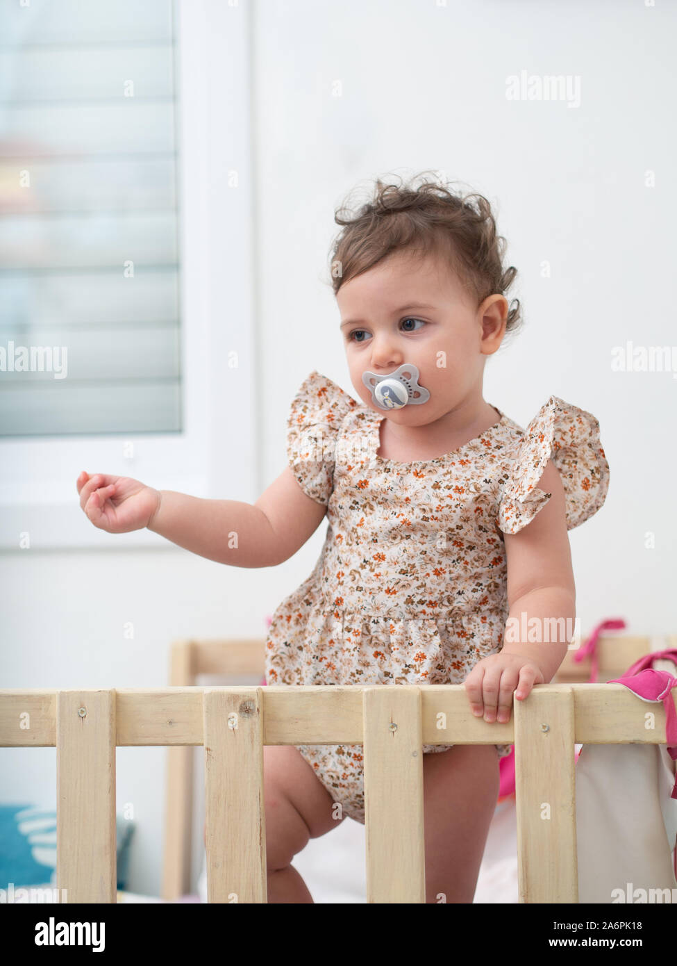 1 year old baby girl stands in her cot (or crib) Stock Photo