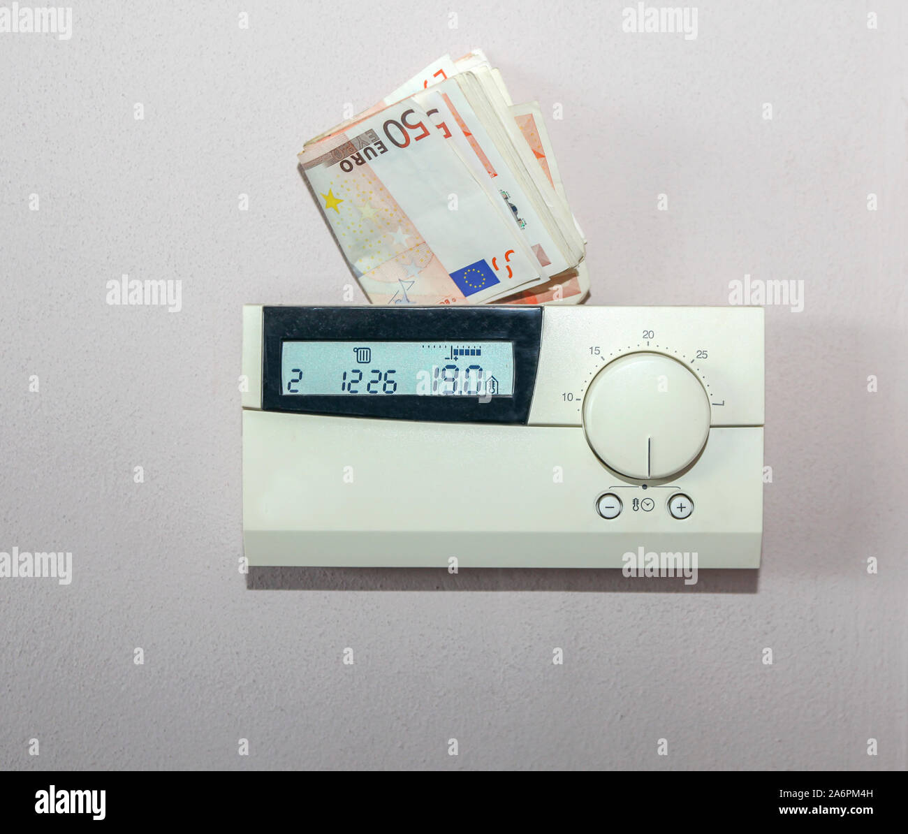 Euro bills behind the thermostat of the central heating system. Concept for the costs of energy Stock Photo